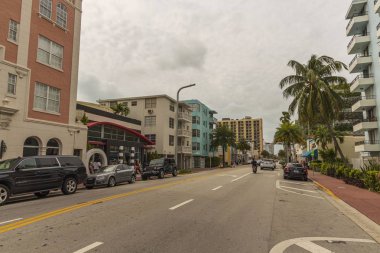 Miami Sahili 'nin güzel manzarası. Asfalt yolun her iki tarafında beyaz binalar ve palmiye ağaçları mavi gökyüzünde ve beyaz bulutlar arka planda. Usa. Miami Güney Sahili. 09.22.2019.