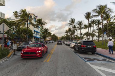 Miami Sahili 'nin güzel manzarası. Beyaz binalar, arabalar ve asfalt yolun her iki tarafında palmiye ağaçları mavi gökyüzünde ve beyaz bulutlar arka planda. Usa. Miami Güney Sahili. 09.24.2019.