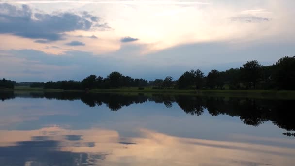 Au ralenti. Vue magnifique sur le coucher du soleil lors d'une soirée d'été calme. Rive du lac avec des arbres verts et des plantes se reflétant dans la surface de l'eau miroir cristalline. Ciel couvert de gros nuages de tonnerre .