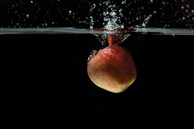 Siyah arka planda suya düşen renkli elmanın yakın görüntüsü. Muhteşem arka planlar..