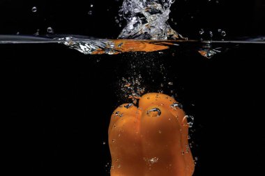 Siyah arka planda suya düşen renkli sarı biberin yakın görüntüsü. Muhteşem arka planlar..