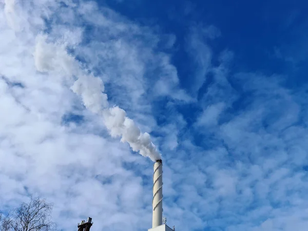 View of white smoke from chimney on blue sky background. Ecology and greenhouse effect concept.