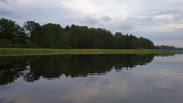 穏やかな夏の夜に夕日の豪華な景色 透き通った鏡面に反射する緑の木々や植物と湖の海岸 激しい雷雲に覆われた空 スローモーション — ストック動画