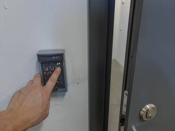 Close up view of male hand dialing code on digital lock near gray steel door. Safety concept.