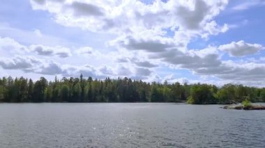 Güzel doğa manzarası. Kayalık kıyı şeridi, mavi su yüzeyi ve beyaz bulutlu mavi gökyüzünde yeşil ağaçlar. İsveç, Avrupa.