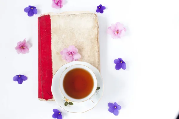 Romantic background with cup of tea lilac flowers and retro book over white table . — Stock Photo, Image