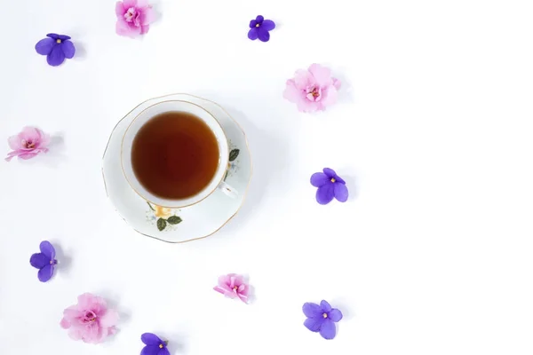 Tasse de thé et branche de petites fleurs roses sur table blanche — Photo