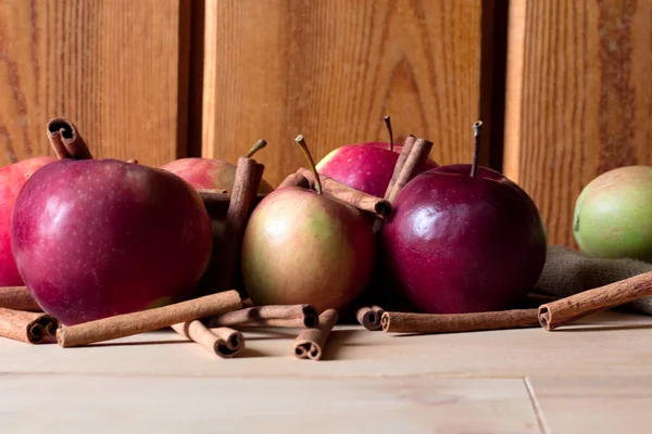 Ripe apples with cinnamon sticks on wooden table, on bright background