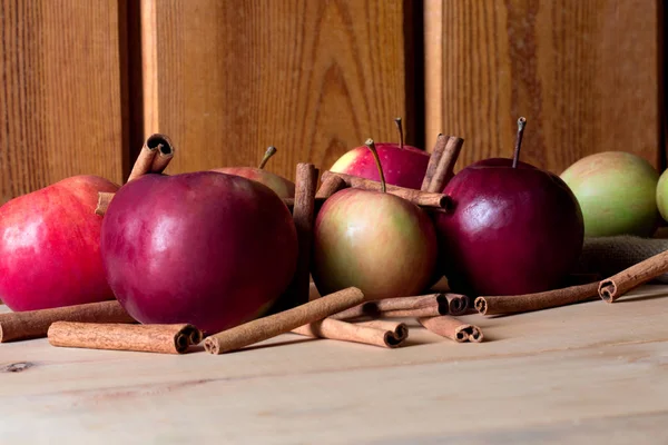 Mogna röda äpple och kanelstänger på trä bakgrund — Stockfoto