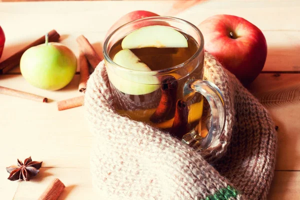 Tazza trasparente con bevanda calda e mela avvolta in una sciarpa riscaldante su un tavolo di legno — Foto Stock
