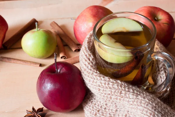 Genomskinlig kopp med varm dryck och apple insvept i en värmande halsduk på ett träbord — Stockfoto