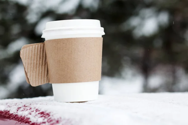 Ångande kopp av kaffe eller te stående på tabellen utomhus i snöiga vintermorgon. Mysiga festliga papper cupwith en varm dryck i vinterträdgården. Christmas Morning koncept . — Stockfoto