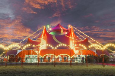 Night view of a circus tent under a warn sunset and chaotic sky