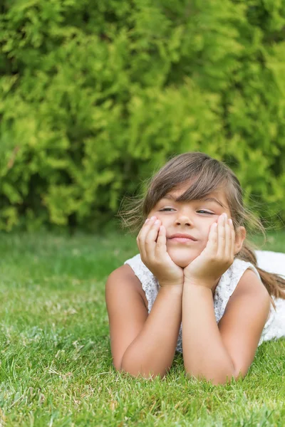 Attraktives kleines Mädchen auf dem Rasen liegend. vertikal. — Stockfoto