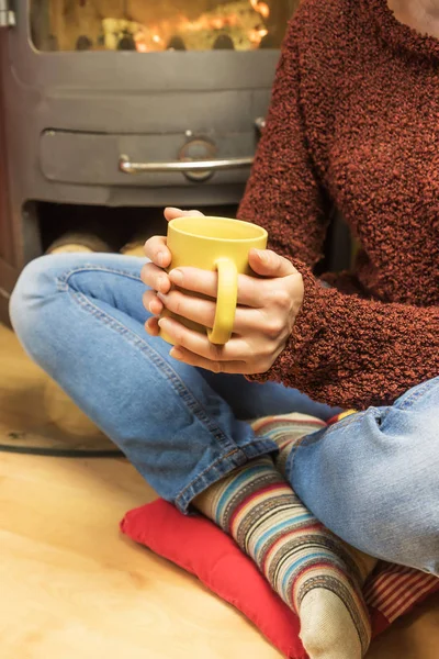 Soba yanan önünde çay kupa ile oturan kadın.