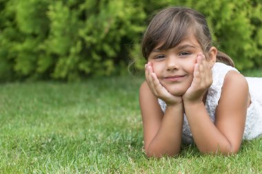 Gülümseyen esmer küçük kız çim üzerinde yalan 