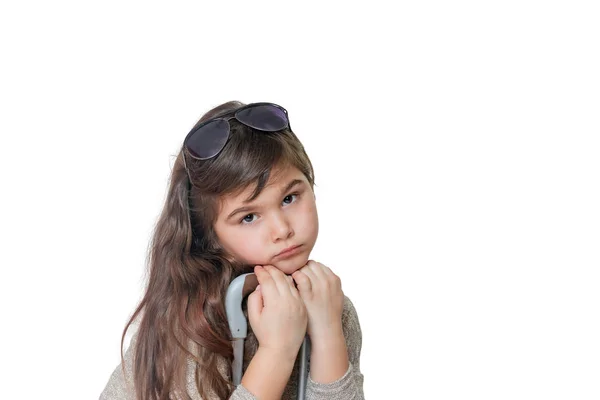 Sad little girl is leaning on the handle of a suitcase and looki — Stock Photo, Image