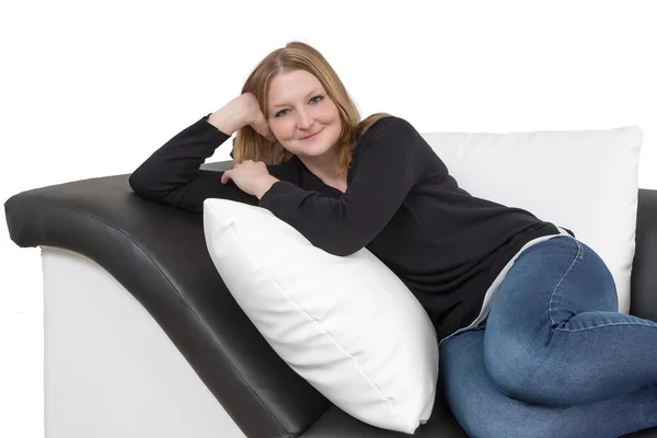 Sorrindo jovem mulher está deitada em um sofá preto e branco — Fotografia de Stock