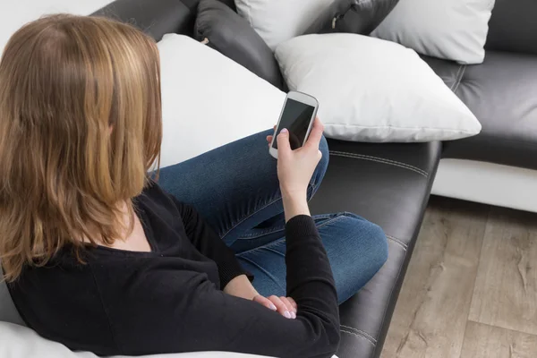 Rückansicht einer jungen Frau, die mit ihrem Smartphone auf einem Sofa sitzt — Stockfoto