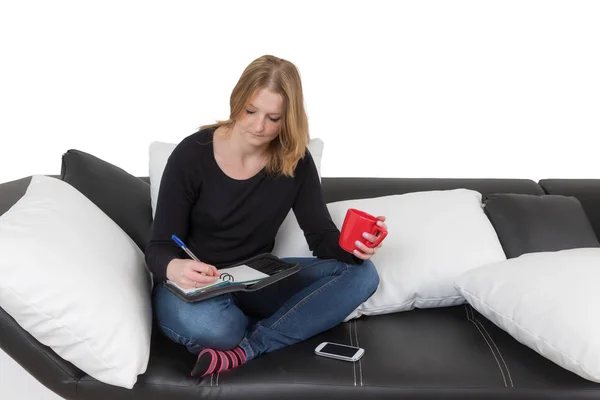 Giovane donna sta scrivendo nel suo diario seduta su un divano — Foto Stock
