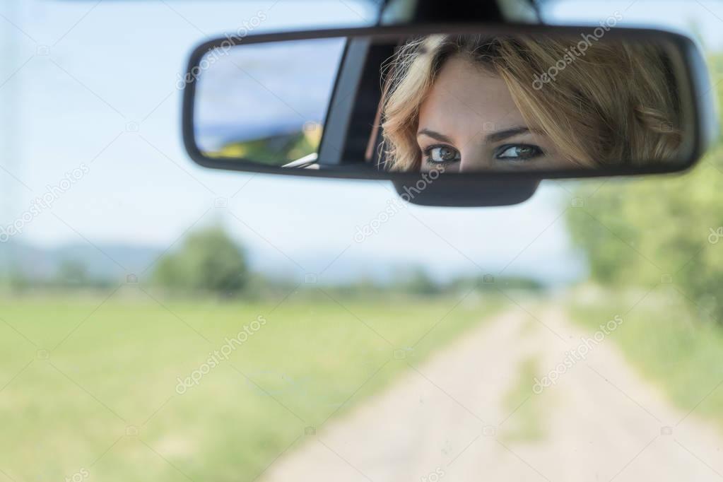 The eyes of the young driver woman are reflected in the rearview