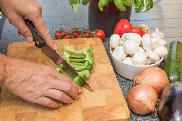 Side view of woman slicing a green paprika on a wooden board — Stock Photo, Image