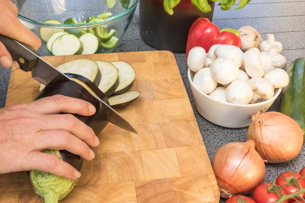 Side view of woman slicing a eggplant on a wooden board — Stock Photo, Image
