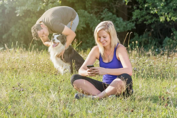 Jonge vrouw is met behulp van slimme telefoon terwijl haar partner wi speelt — Stockfoto