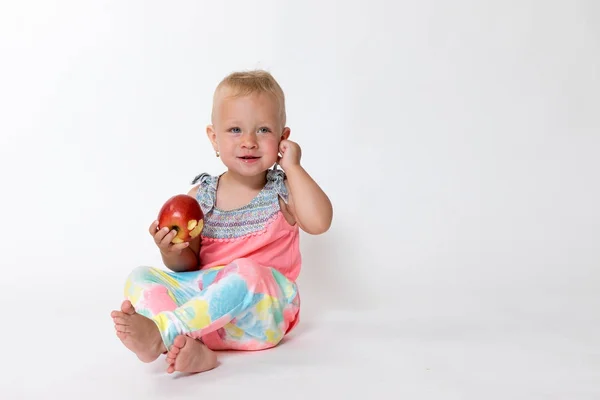 Whole figure of smiling toddler girl sitting and holding red ap — Φωτογραφία Αρχείου