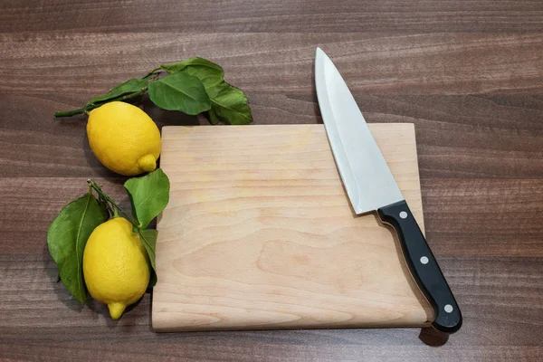 Mesa de cozinha com faca e dois limões com folhas verdes — Fotografia de Stock
