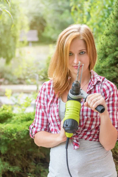 Attraente giovane donna sta mostrando trapano elettrico all'aperto. Verti — Foto Stock