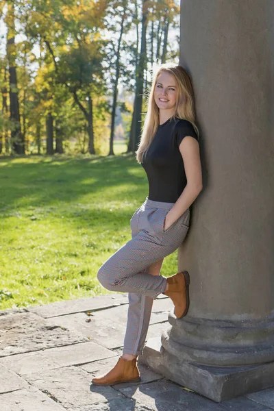 Χαμογελώντας όμορφο κορίτσι στέκεται ακουμπώντας σε μια κολώνα το φθινόπωρο — Φωτογραφία Αρχείου