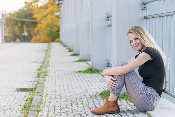 Krásná mladá dívka sedí na mostě a usmívá se na kameru — Stock fotografie
