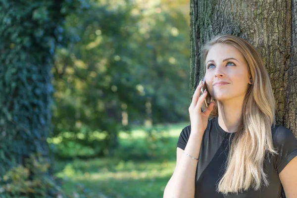Usmívající se atraktivní mladá dívka je telefonování v parku — Stock fotografie