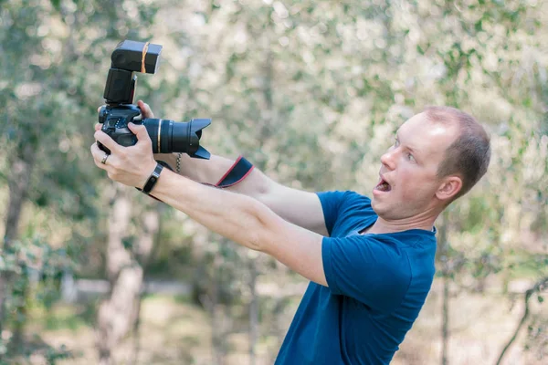 Funny guy got scared of the DSLR camera holding it in his hands on summer day. Joke picture of beginners in career of photographer.