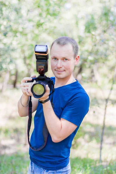 Portret van aantrekkelijke mannelijke fotograaf met blauw t-shirt buitenshuis op zomerdag. Jonge man met een Dslr camera in handen — Stockfoto