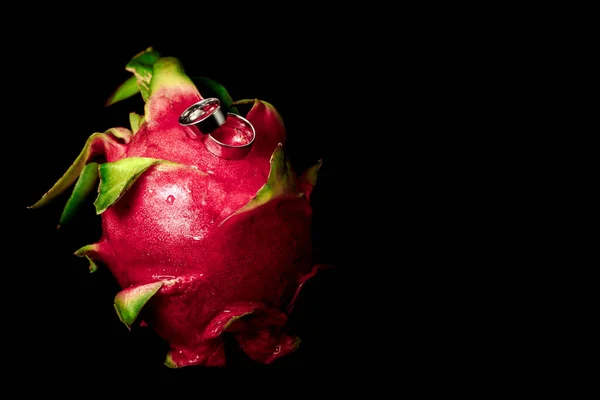 Beyaz altından alyanslar yakın plan, siyah arka plan egzotik meyveler.