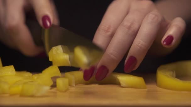 Primer plano de las manos de la mujer cortando pimiento amarillo en el tablero de madera en una cocina moderna . — Vídeos de Stock