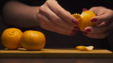 Kadın ellerine yakın çekim modern bir mutfaktaki ahşap tahtada mandalinayı arındırır. Sağlıklı beslenme.