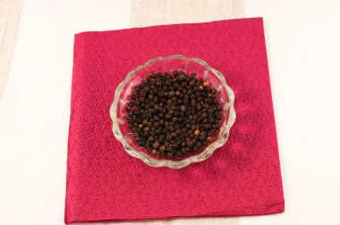 Bir cam tabakta kağıt peçete bordo renk arka plan üzerinde siyah kuru biber bezelye.