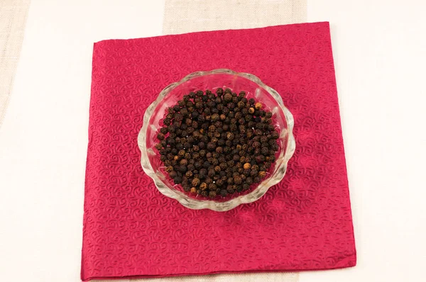 Bir cam tabakta kağıt peçete bordo renk arka plan üzerinde siyah kuru biber bezelye.