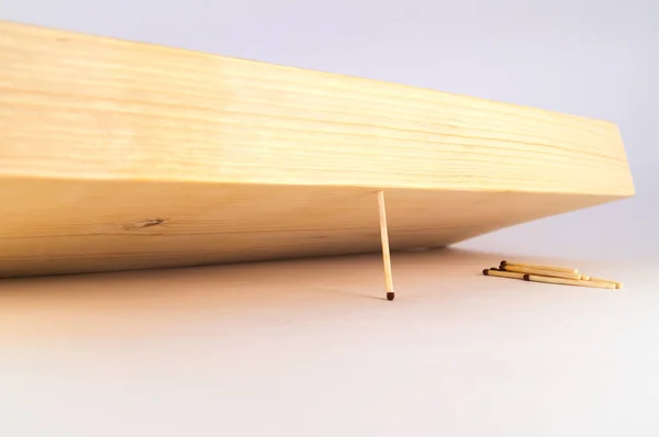 A thin match keeps the massive wooden board from falling, preventing it from falling on the remaining matches.