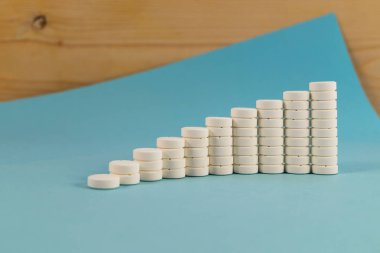 Beyaz yuvarlak tablet hap her sayısında aşamalı bir artış ile sütunlarda maruz, sonraki çerçevede bir mavi arka plan ve Ahşap dokusu.