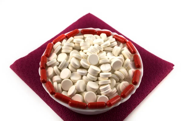 白い背景に医学と赤いカプセルの縁の縁に沿って 磁器のカップに丸い白い錠剤 — ストック写真