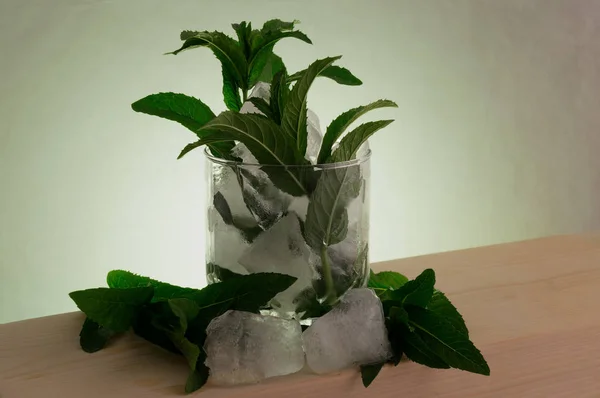 Leaves of green mint with chunks of crushed ice on a wooden surface in backlight.