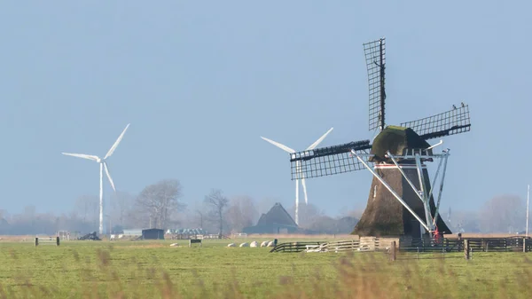 Старая мельница с современными ветряными мельницами на заднем плане — стоковое фото