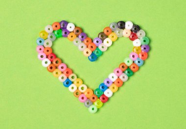 Yeşil üzerinde izole edilmiş, yuvarlak plastik parçalardan kalp.