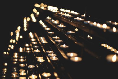 Kilisede dua eden bir sürü mum ışığı olan karanlık bir arka plan.