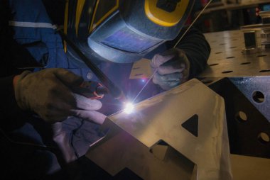 man is welding tig mode an alluminium letter, he is concentrate on his work. clipart