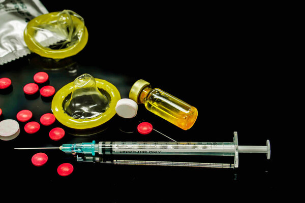 Vaccines in vial,  white and red  medicines with a plastic syringe and condoms isolate on black background. Sample of what caused the HIV infection. and The condom is to prevent infection.